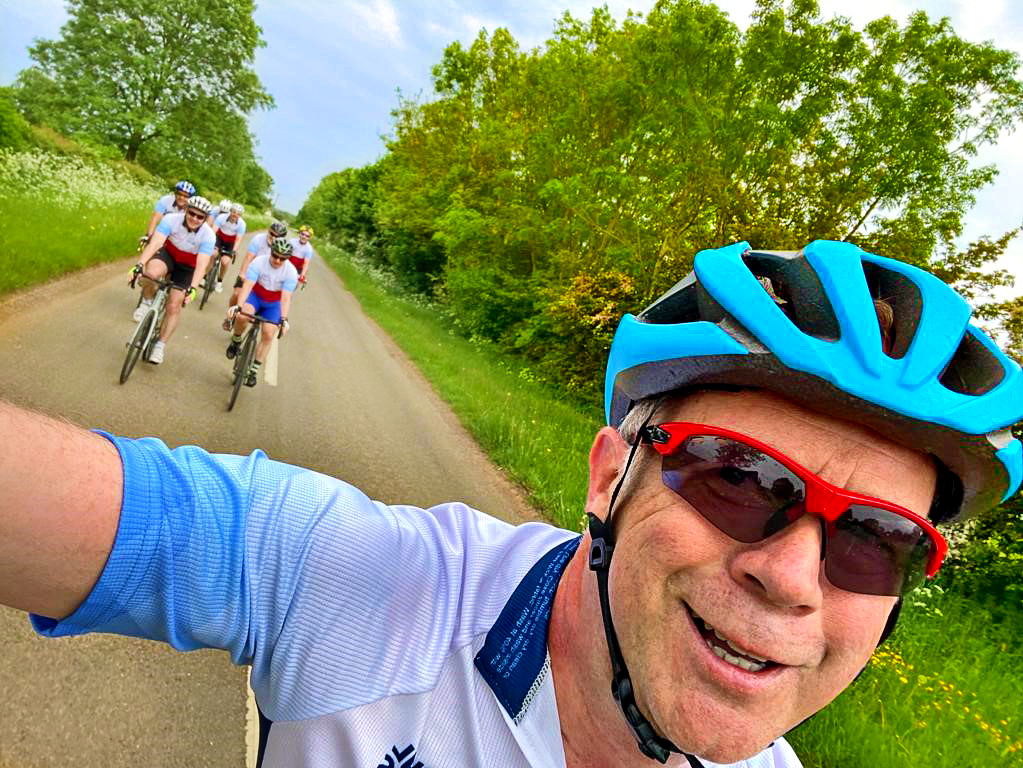 Cyclist takes selfie on the bike, followed by other riders.